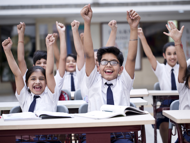 Group of excited school children cheering in classroom
