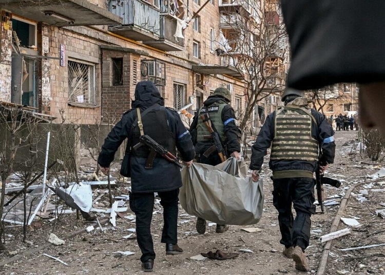 Ukrainian policemen carry a body away from a five-storey residential building that partially collapsed after a shelling in Kyiv on March 18, 2022, as Russian troops try to encircle the Ukrainian capital as part of their slow-moving offensive. - Authorities in Kyiv said one person was killed early today when a downed Russian rocket struck a residential building in the capital's northern suburbs. They said a school and playground were also hit. (Photo by Sergei SUPINSKY / AFP)